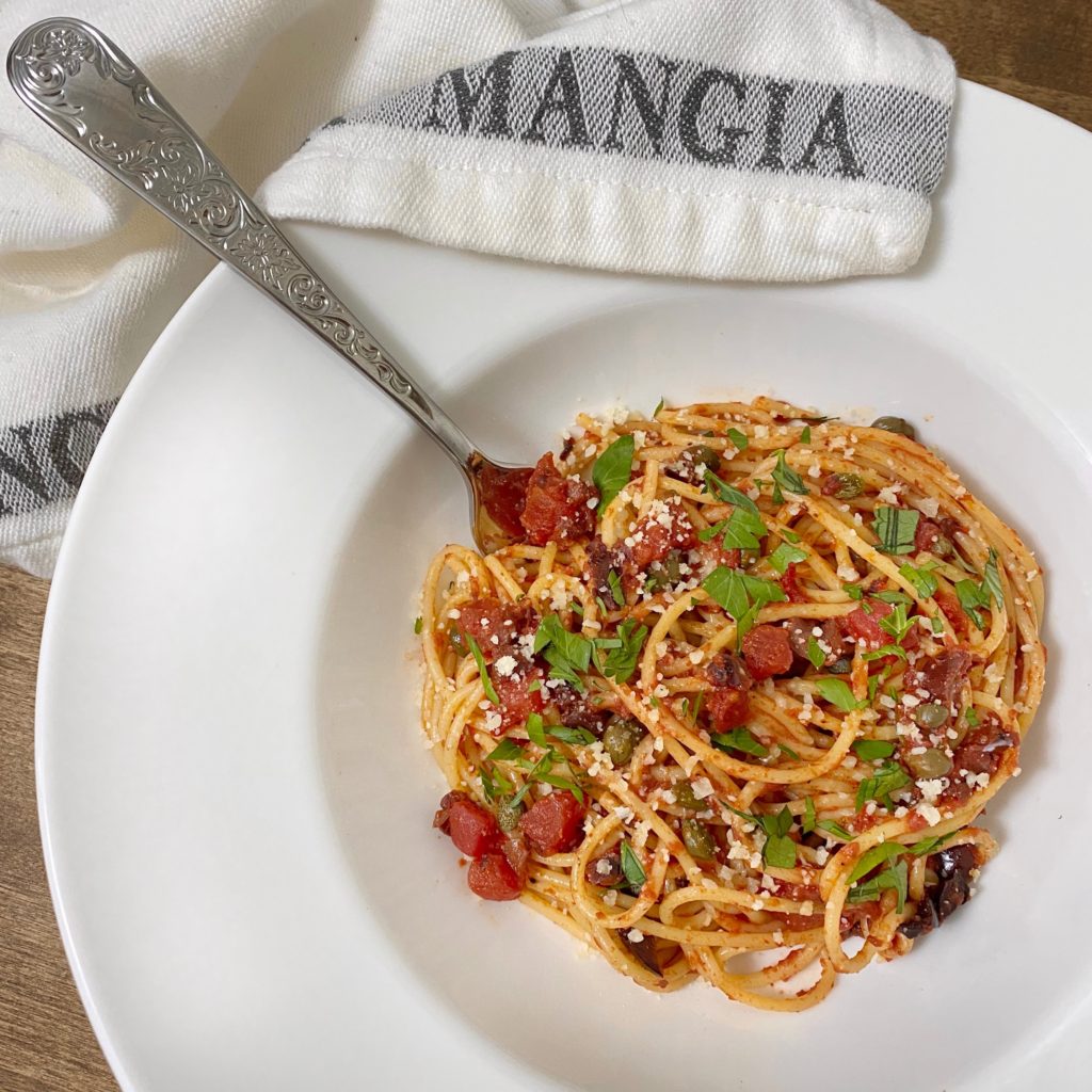 Pasta Puttanesca pasta sauce in a white bowl with a napkin that says "Mangia"